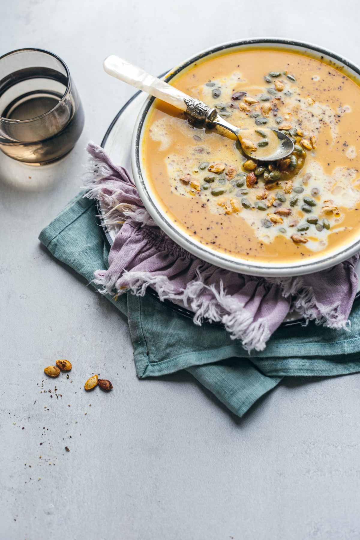 Butternut squash soup with carrots and ginger in a bowl and topped with coconut milk and pumpkin and squash seeds