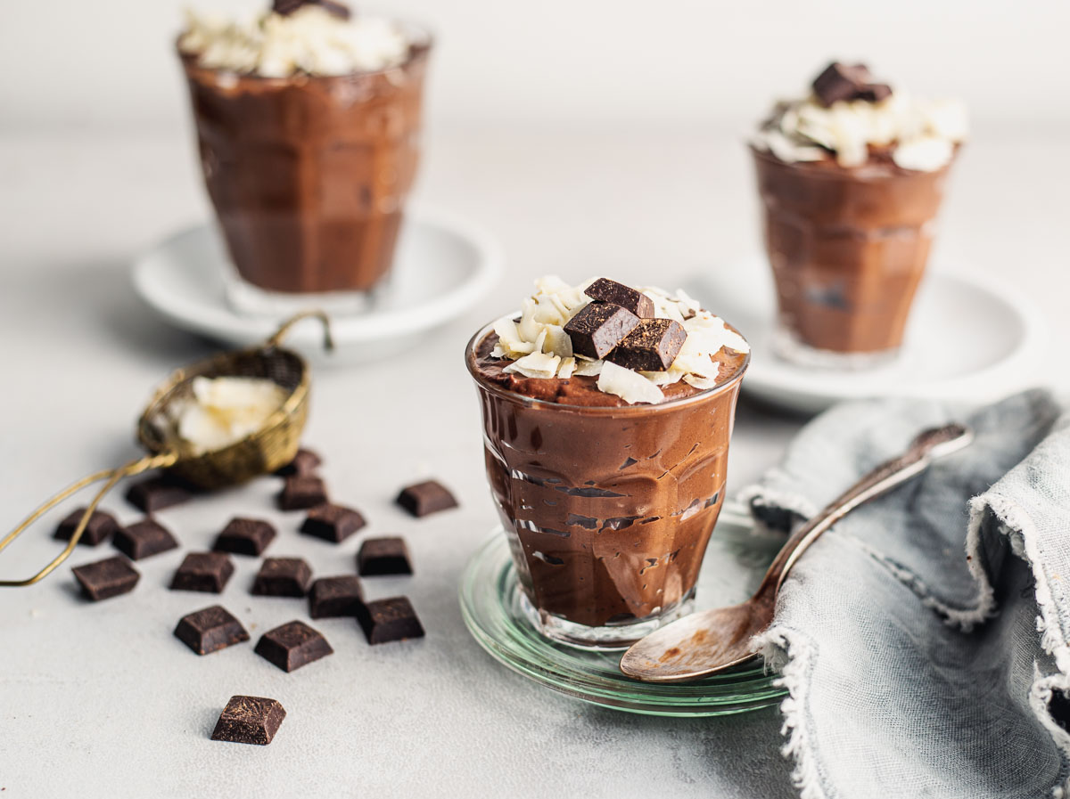 Trois petites tasses à expresso avec mousse au chocolat soyeux à base de tofu mou garnie de flocons de noix de coco et de morceaux de chocolat.