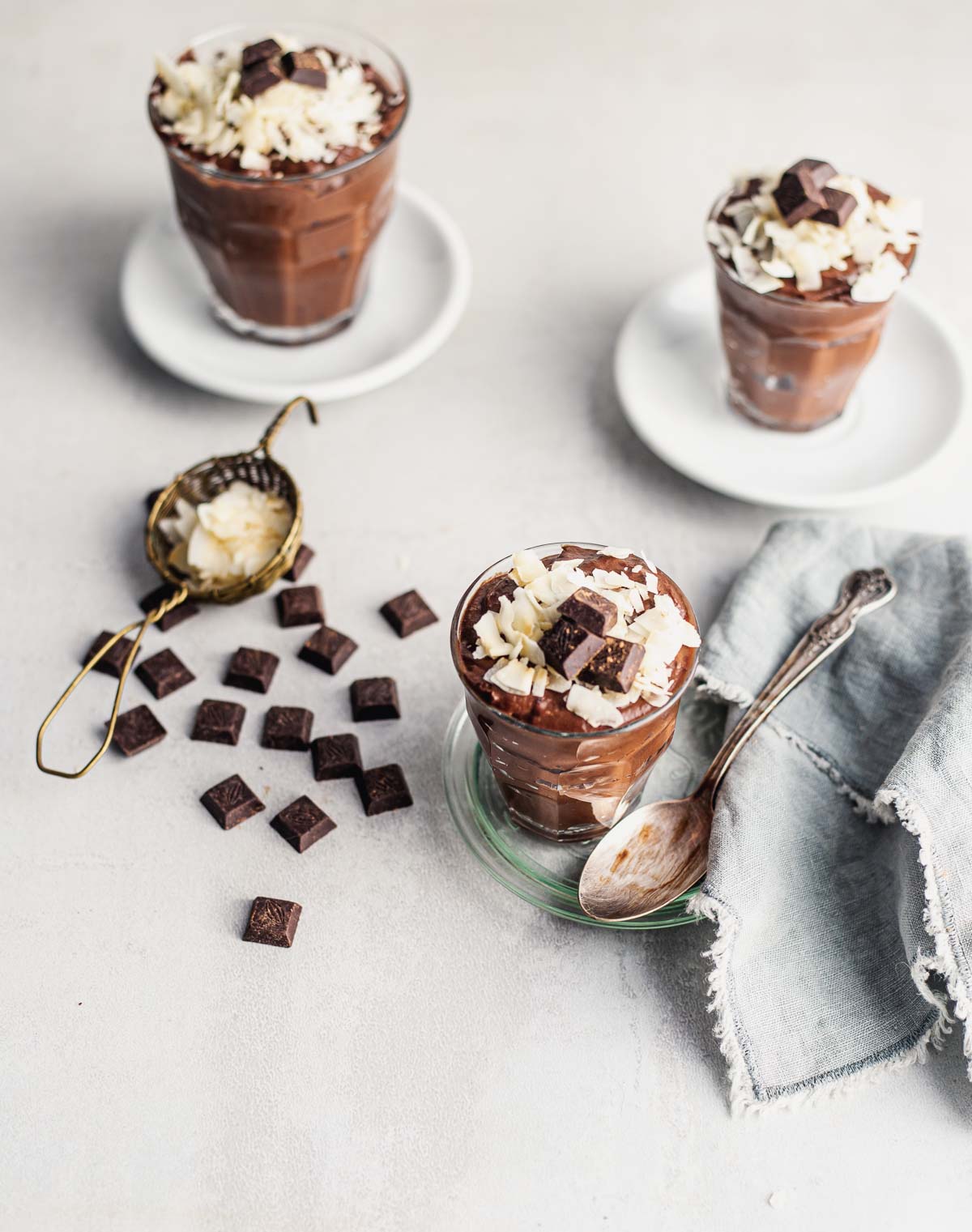 Three small espresso cups with silken chocolate mousse made topped with coconut flakes and pieces of chocolate.