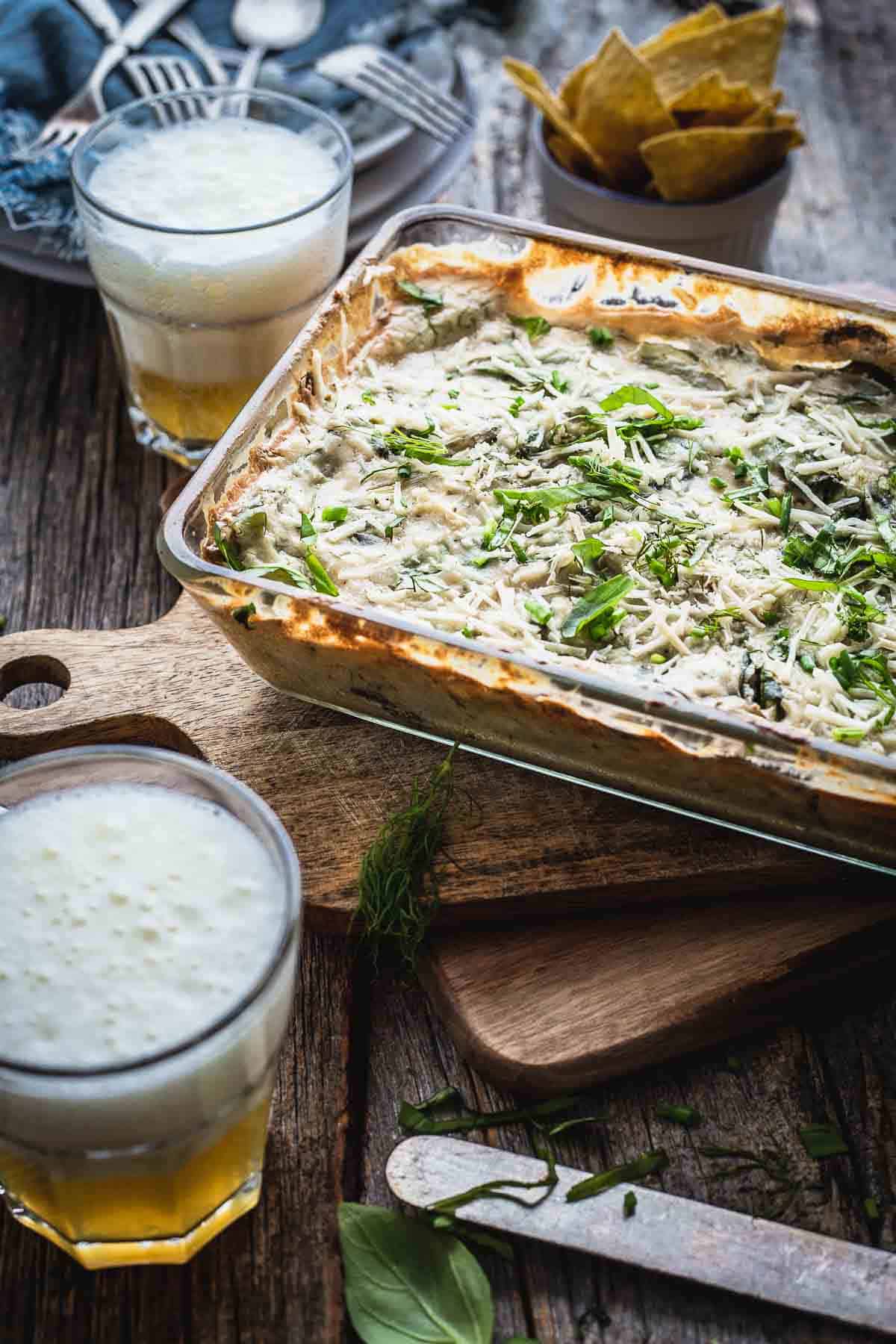 Spinach Artichoke Dip in a baking dish and tortilla chips next to it and a glass of beer.