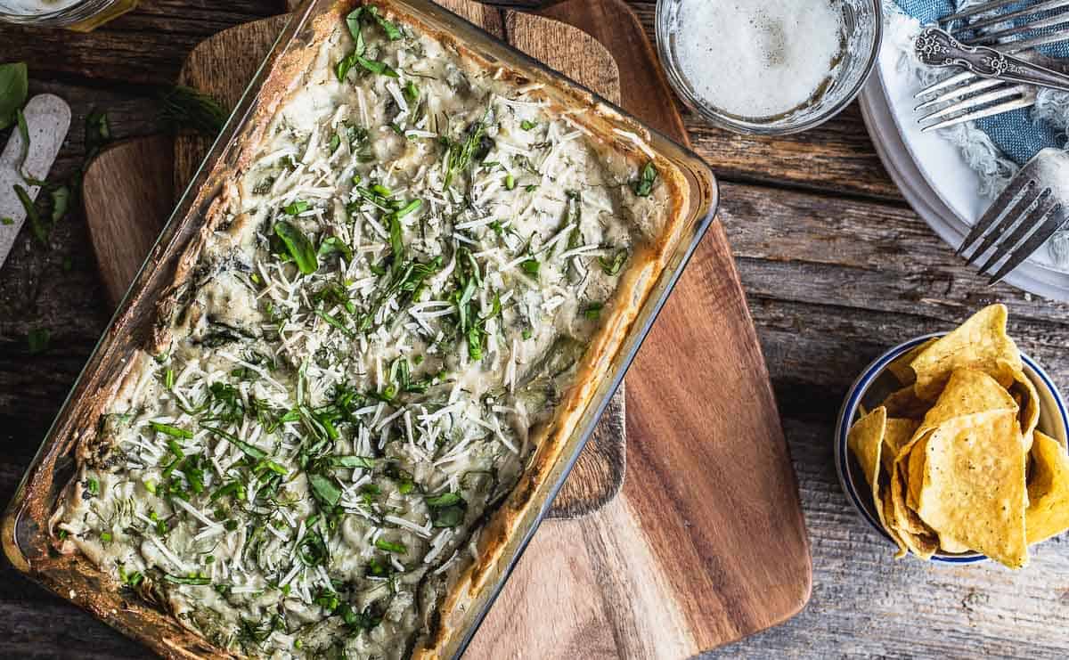 Spinach Artichoke Dip in a baking dish and tortilla chips on its right.