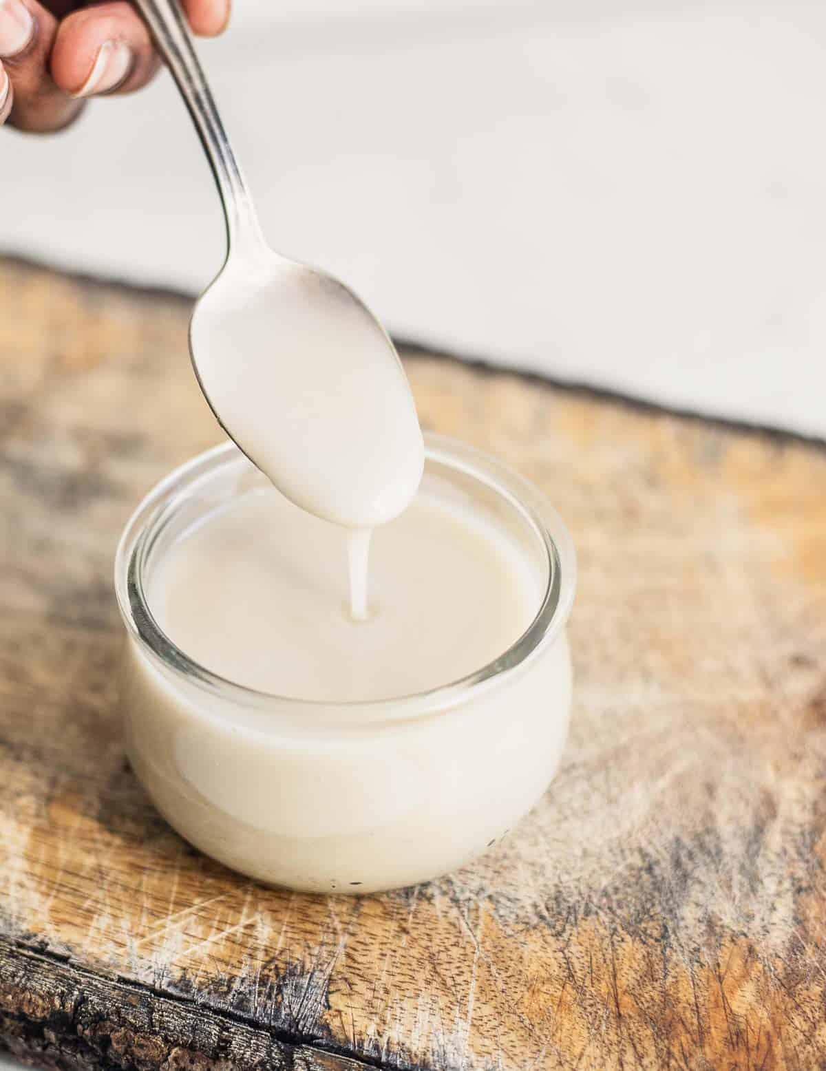 Sweetened condensed milk being poured with a spoon into an airtight jar.