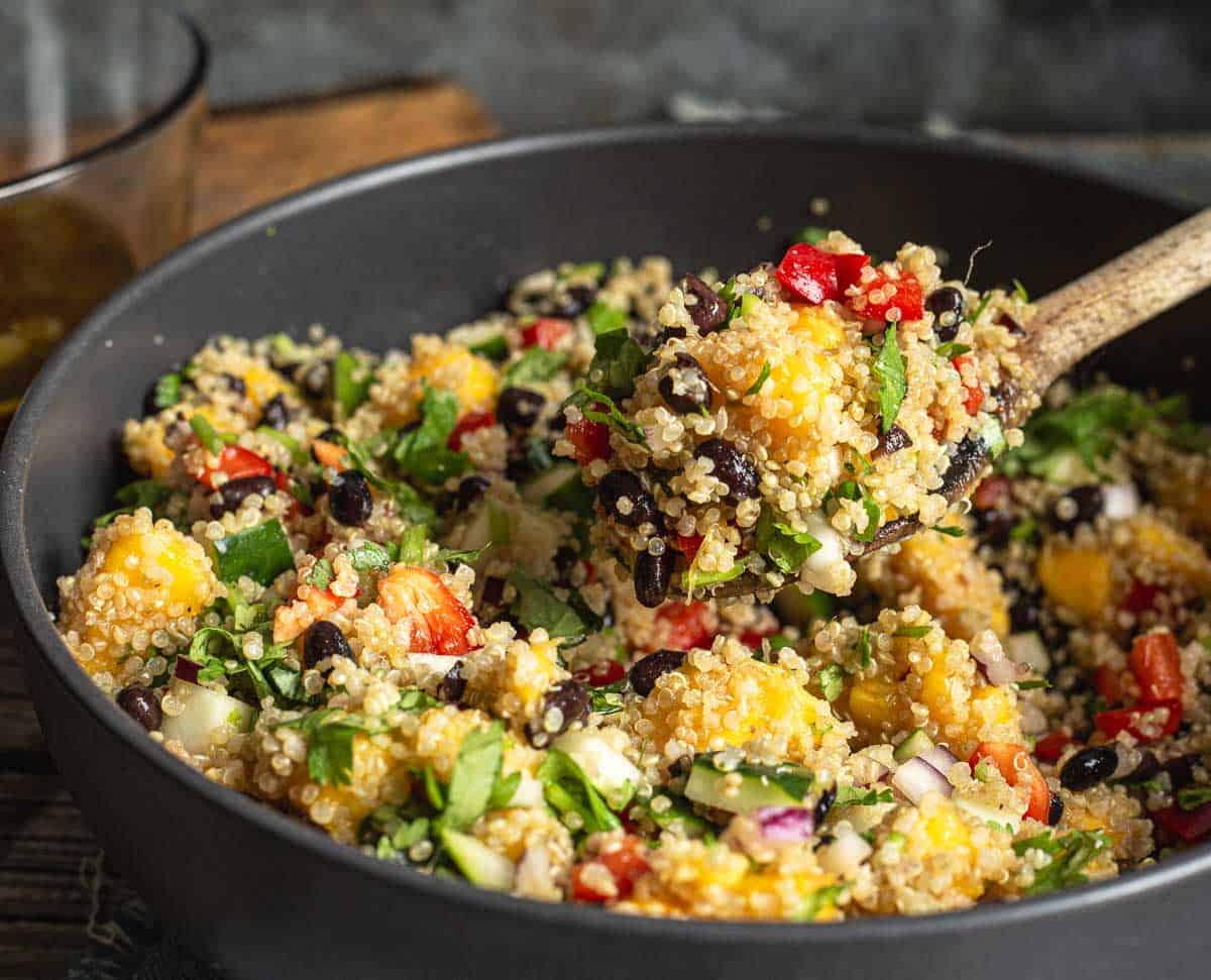 Mango quinoa salad scooped by a wooden spoon.